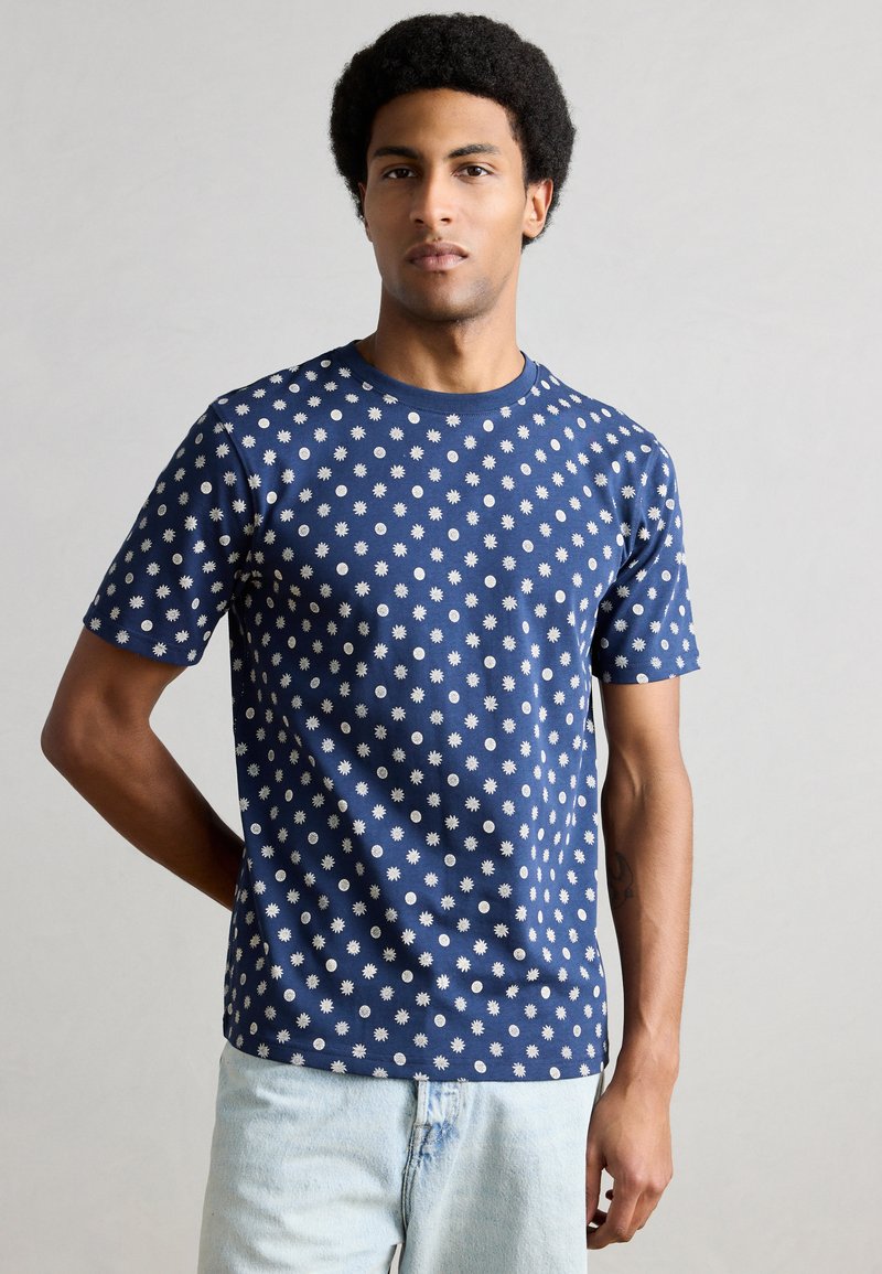 Μπλε βαμβακερό T-shirt σε σκούρο ναυτικό χρώμα με λευκά κυκλικά και ανθισμένα σχέδια, κοντά μανίκια και στρογγυλή λαιμόκοψη. Κλασική εφαρμογή με λεία υφή.