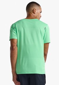 Camiseta deportiva verde fabricada con material ligero y transpirable. Presenta una superficie texturizada con ligeras perforaciones y mangas cortas.