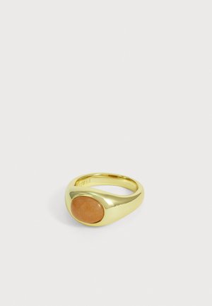 Bague en or avec une pierre orange ovale lisse sertie dans un anneau poli simple sur un fond clair uni.