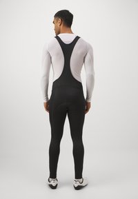 Schwarze Radsport-Bib-Shorts mit figurbetontem Design und Mesh-Rückenteil. Der Stoff wirkt matt und verfügt über eine Tasche im Sitzbereich.