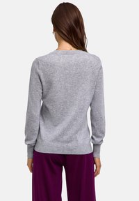 Grau gestrickter Pullover mit langen Ärmeln, Rundhalsausschnitt und geripptem Saum. Weiche Textur; Modell trägt ihn mit lila Hosen.