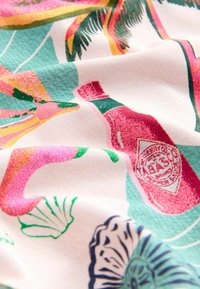 Tela colorida con un diseño impreso que incluye elementos en rosa, verde y azul, como una botella y motivos tropicales sobre un fondo claro.