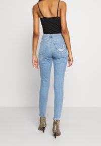 Vaqueros de cintura alta en un azul claro con un ajuste ceñido, con bolsillos traseros y detalles desgastados, combinados con una camiseta negra ajustada y botas de tacón.