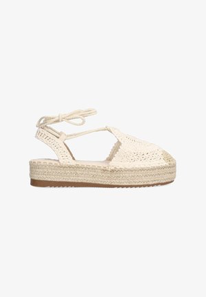 Sandalia de esparto beige con parte superior trenzada, cintas ajustables en el tobillo y una suela de yute gruesa. La punta redondeada y los detalles texturizados realzan el diseño.