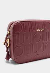 Borsa a mano in pelle bordeaux con superficie testurizzata e dettagli del logo impressi. I materiali in oro evidenziano il design. Chiusura con zip nella parte superiore.