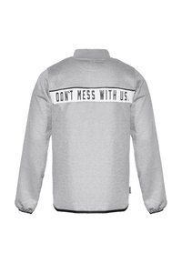 Lys grå jakke med lange ermer, elastiske mansjetter og svart tekst "IKKE KØR MED OSS." over øvre del av ryggen på en hvit stripe.