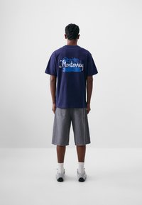 Camiseta de manga corta azul marino con "Monterrey" en un script blanco sobre un fondo azul; combinada con pantalones cortos de mezclilla grises y zapatillas.