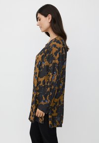 Blusa de manga larga con un patrón floral en marrón, negro y azul, que presenta un corte holgado y un escote redondo con detalles fruncidos.
