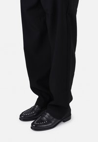 Black leather loafers featuring decorative studs and a smooth finish, paired with loose black trousers.