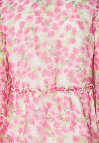 Robe fleurie en tissu léger et transparent avec une base blanche et un motif floral rose. La taille à volants souligne le design.