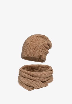 Beige Strickmütze mit strukturiertem Blättermuster und passendem geripptem Schal. Beide Teile sind mit einem subtilen Markenlabel auf der Mütze versehen.