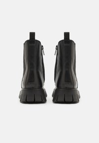 Botines negros con un acabado de cuero suave, cremalleras laterales y suelas de goma texturizadas que presentan un distintivo patrón en zigzag.