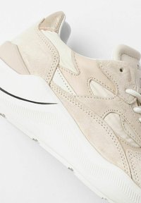 Sneaker in suede beige con accenti testurizzati, suola intermedia bianca e dettagli a strisce nere. Presenta un collo imbottito e un design con lacci.