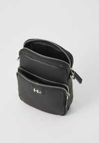 Sac en cuir noir avec deux compartiments zippés, quincaillerie argentée, surface texturée et un logo à l'avant. Forme compacte et carrée.