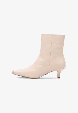 Bežīgas ādas potītes zābaki ar smailu purngalu, zelta purngala apdari un zemu papēdi. Gluda tekstūra un eleganta forma uzsver tā mūsdienīgo izskatu.