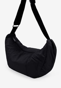 Bolso de hombro de tela negra con forma suave y redondeada, que cuenta con un cierre de cremallera y una correa ajustable para mayor comodidad.