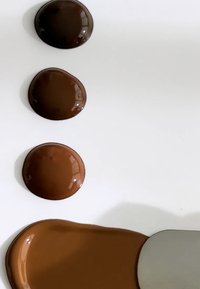 Tre blanke, runde klatter med mørkebrunt maling, ordnet vertikalt på en hvit overflate, med en metallpalettkniv som glir gjennom bunnen.