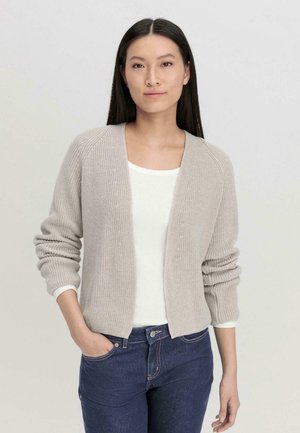 Gestrickte Cardigan in Hellgrau, offen, mit geripptem Muster, langen Ärmeln und umgeschlagenen Bündchen. Darunter ein weißes T-Shirt, kombiniert mit dunklen Jeans.