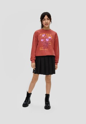Sweat-shirt cramoisi avec graphique floral et texte, associé à une jupe plissée noire et des bottes de combat noires à lacets.