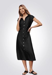 Vestido midi negro de botones con cuello y mangas cortas. Presenta un corte recto, textura suave y botones de color claro.