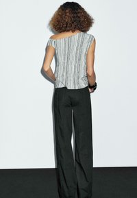 Gestreepte off-shoulder top in zwart en witte stof, gecombineerd met losse zwarte broek. De top heeft een asymmetrische zoom en een subtiele textuur.
