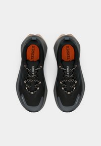 Μαύρα αθλητικά παπούτσια με υφασμένη επένδυση, που διαθέτουν πορτοκαλί εσωτερική σόλα, καφέ λεπτομέρειες και κορδόνια σε αντίθεση. Σχεδιασμένα για υπαίθριες δραστηριότητες.