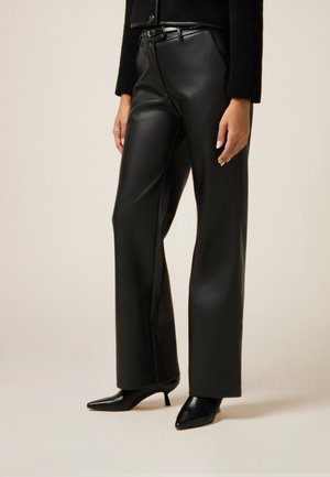 Pantalones de cuero negro con una cintura alta, diseño de pernera recta, combinados con zapatos negros de punta. Textura suave y detalles mínimos.