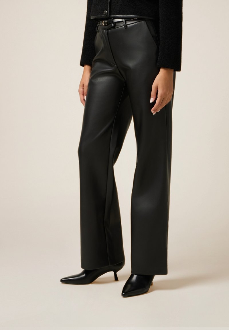 Zwarte leren broek met een hoge taille, recht gesneden ontwerp, gecombineerd met puntige zwarte schoenen. Glad textuur en minimale details.