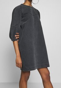 Överdriven grå denimklänning med rund halsringning, puffärmar och synliga sömnadsdetaljer. Slät textur och knälång design.