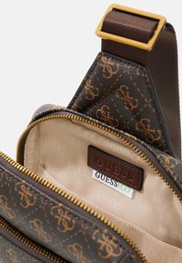 Borsa in pelle marrone con motivo, dotata di hardware tono oro, chiusura con zip e interno beige con etichetta del logo.