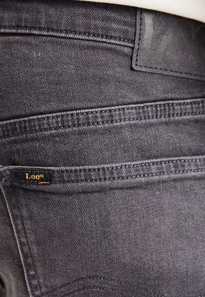 Gros plan sur la poche arrière d'un jean en denim noir avec une petite étiquette de la marque Lee et une pièce en cuir cousue à la taille.