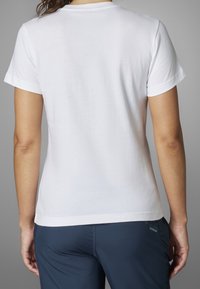 Valkoinen puuvillainen t-paita, jossa on lyhyet hihat, pyöreä pääntie, sileä pinta ja yksinkertainen muotoilu, yhdistetty laivastonsinisiin housuihin, joissa on logokoriste.