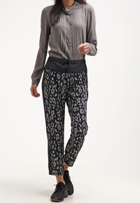 Lysegrå langærmet bluse med plisseringer; sorte træksnorsbukser med et farverigt leopardmønster; parret med sorte sneakers.