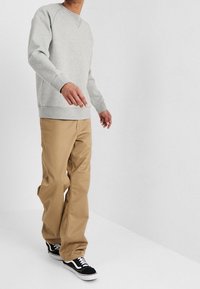 Szara bawełniana bluza typu crewneck, połączona z beżowymi spodniami szerokimi i czarnymi trampkami z białą podeszwą, na neutralnym tle.