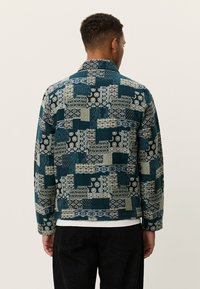 Μπουφάν με πουά ραφές σε συνδυασμό αποχρώσεων τιρκουάζ, γκρι και μαύρου. Το υφασμά του με υφή διαθέτει γεωμετρικά και λουλουδάτα σχέδια. Στυλ με γιακά, μακριά μανίκια.