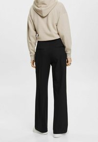 Svarta vida byxor med hög midja, har två bakfickor och är ihopparade med en beige hetsare med huva. Slät, strukturerad tyg.