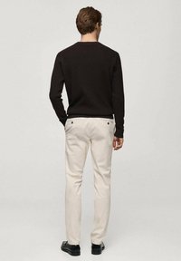 Pull côtelé marron foncé avec un col rond, associé à un pantalon beige clair doté de deux poches arrière et de boutons noirs. Chaussures noires.