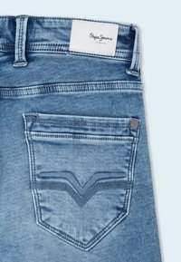 Jeans de mezclilla azul claro con una etiqueta blanca que dice "Pepe Jeans London", un bolsillo trasero con una costura decorativa en forma de V y remache.