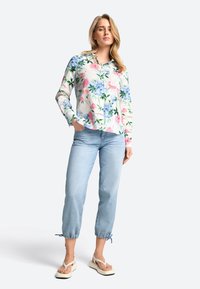 Bloemrijke blouse met lange mouwen in een roze, blauwe en groene print, gecombineerd met lichtblauwe denim cropped broek met strikjes bij de enkels.