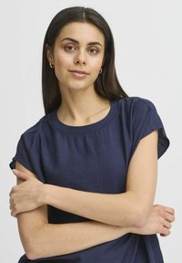 Top blu navy a maniche corte con scollatura rotonda, realizzato in tessuto testurizzato, con una vestibilità ampia e pieghe sottili sulle spalle.
