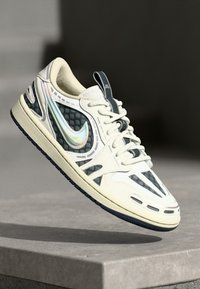 Tenisky Nike v smotanovo-béžovej a námorníckej modrej farbe s textúrovanými čiernymi akcentmi, iridescentným swooshom a jedinečným vzorom výrezov, s gumovou podrážkou.
