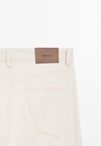 Rückansicht von cremeweißen Jeans aus Denim mit einer einzelnen Gesäßtasche und einem braunen Lederpatch mit dem Aufdruck "Massimo Dutti".
