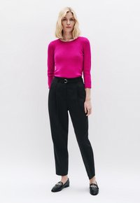 Fuchsia Strukturstrickpullover mit Dreiviertelärmeln, kombiniert mit hochtaillierten schwarzen Stoffhosen und schwarzen Loafers mit goldenen Akzenten.