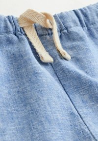 Gros plan sur un pantalon en tissu bleu clair avec une ceinture élastique et un cordon beige en tricot noué au centre devant.