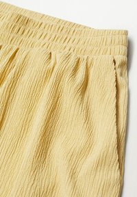 Tissu jaune texturé avec une apparence froissée et une ceinture élastique, montrant des plis doux et des lignes subtiles créées par le tissage.
