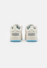 Sneakers PUMA z fakturowaną beżową cholewką, niebieskimi podeszwami i wyraźnym szarym logo na pięcie; posiadają pętelkę z tyłu.