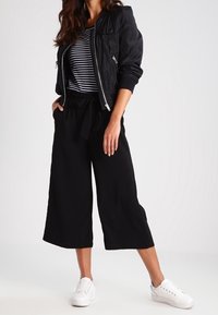 Svart bomberjacka, randig topp, vida svarta culotter och vita sneakers. Slät tyg med avslappnad passform och minimalistisk design.