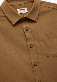 Brązowa, krótka koszula z teksturowanej tkaniny, z kołnierzykiem typu button-down, przednią kieszenią oraz brązowymi guzikami w delikatny wzór w kratkę.