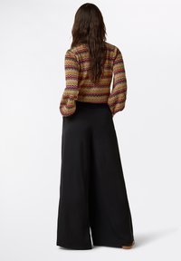 Gemusterte Bluse mit Puffärmeln in vielen Farben; weite schwarze Hose mit glatter Textur. Die Stoffmischungen sorgen für einen lebendigen Look.