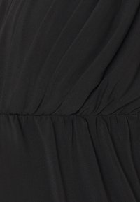 Černá látka s jemnou, lehkou strukturou. Obsahuje sklady a nařasený pas, čímž vytváří plynulý drape.